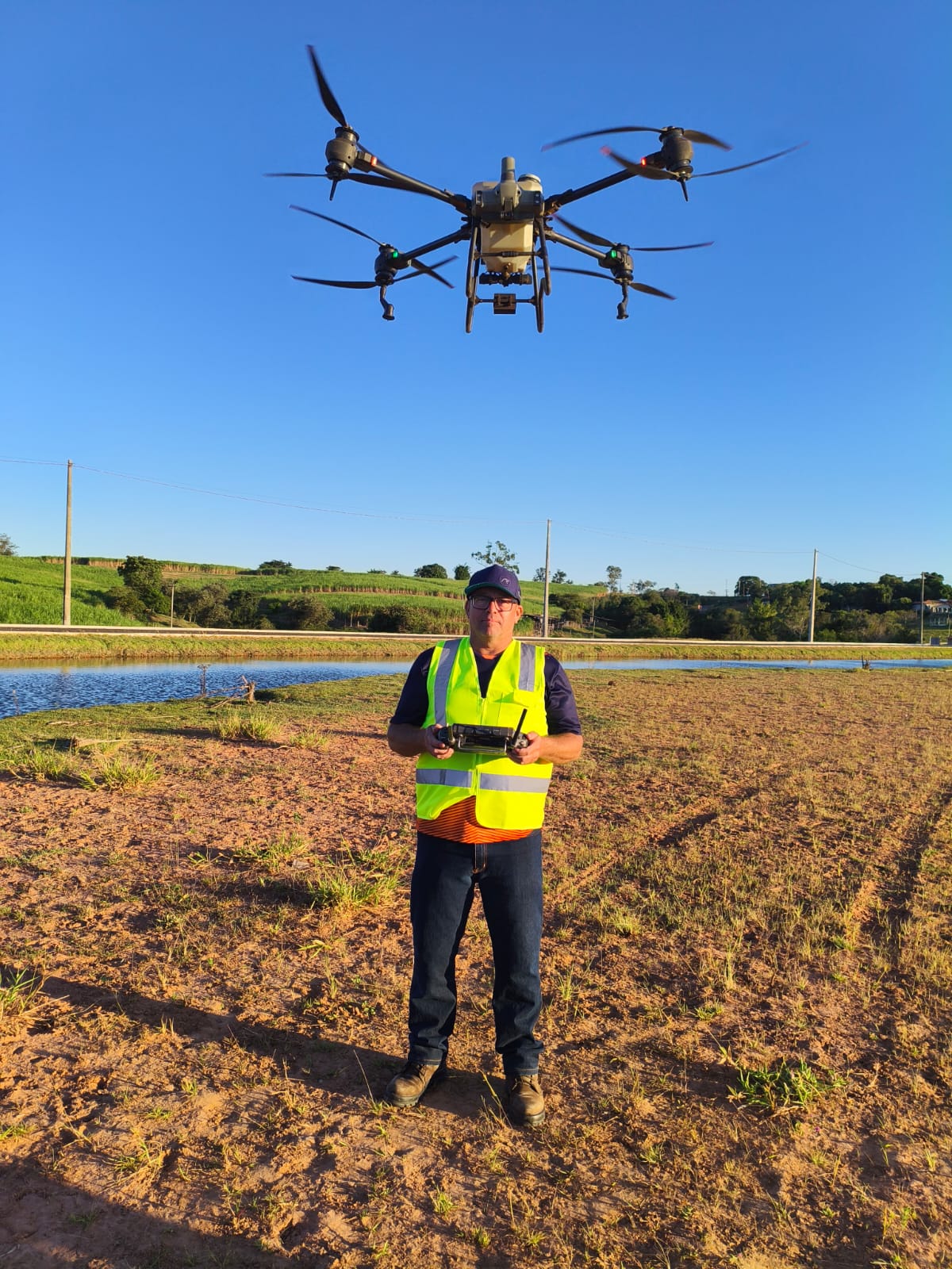 Moisés operando o drone agrícola T55 no campo, com o drone voando acima de sua cabeça